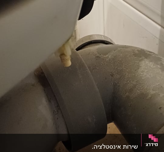 תצלום תקריב של צינורות ניקוז וחיבורי אינסטלציה מתחת לכיור